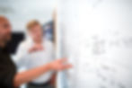 Blurred photo of two people discussing notes on a whiteboard